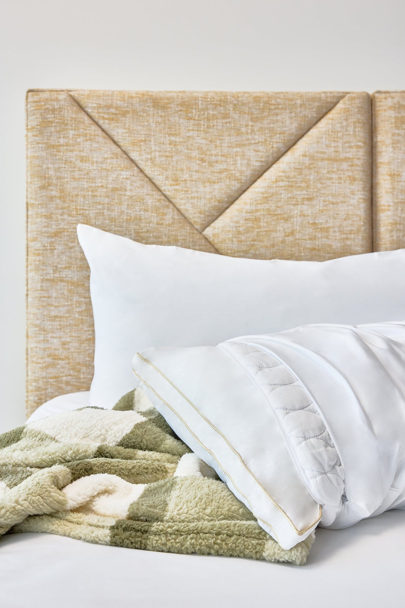 The Lad Collective white pillow with gold trim and green chevron blanket on a gold headboard.