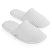 A pair of white ribbed-texture slip-on slippers shown on a clean white background. Shop Meriton Suites.