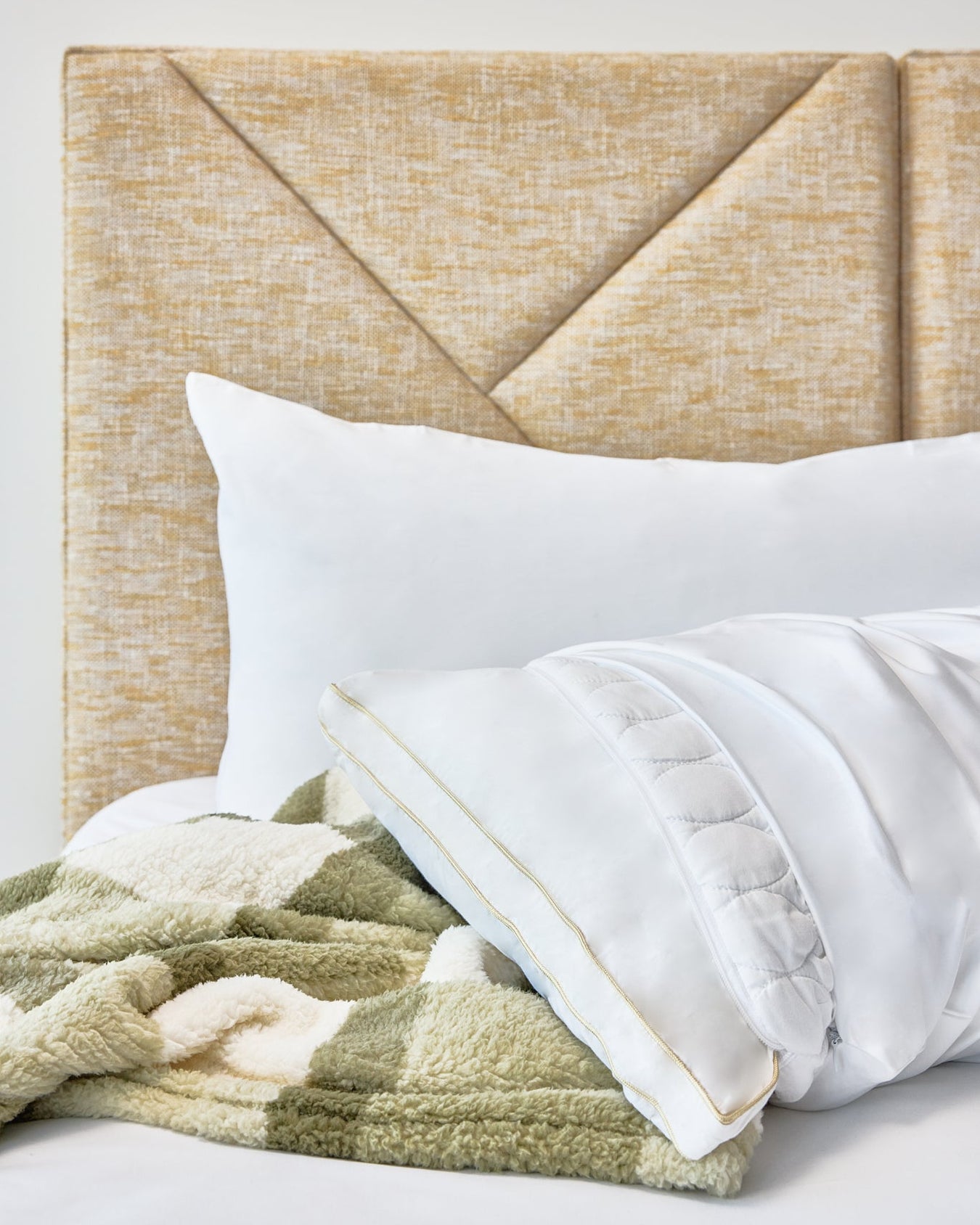 The Lad Collective white pillow with gold trim and green chevron blanket on a gold headboard.