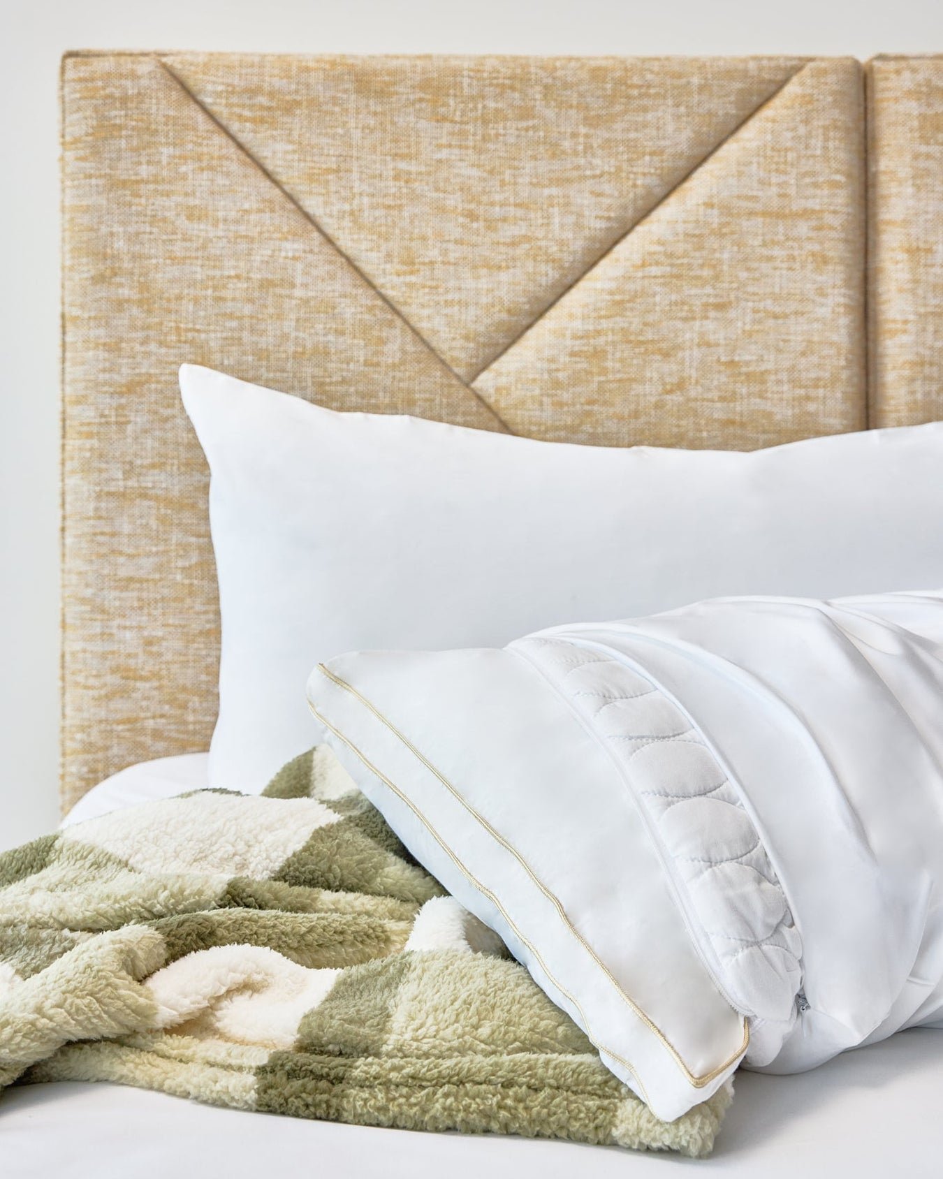The Lad Collective white pillow with gold trim and green chevron blanket on a gold headboard.