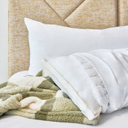 A close-up of a bed with a textured beige upholstered headboard, white pillows, and a soft green and cream checkered throw blanket.