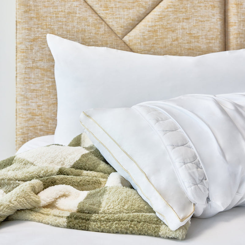 A close-up of a bed with a textured beige upholstered headboard, white pillows, and a soft green and cream checkered throw blanket.