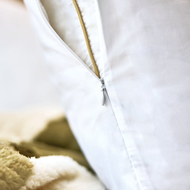 A close-up of a white pillowcase with a gold zipper, resting on a soft beige and olive green sherpa blanket.