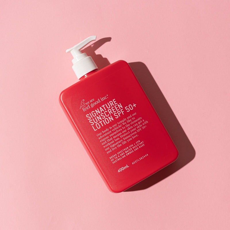A red rectangular pump bottle of WAFGI Signature Sunscreen Lotion SPF 50+ with a white pump, photographed on a solid pink background with a sharp shadow.