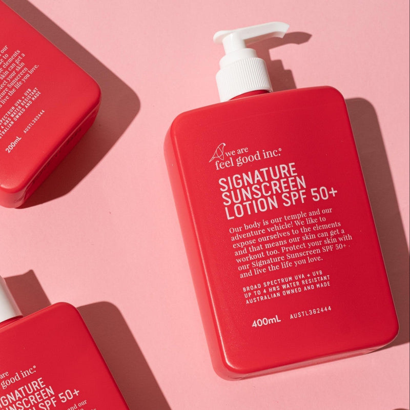 Five red bottles of WAFGI sunscreen and lotion products arranged diagonally on a solid pink background.