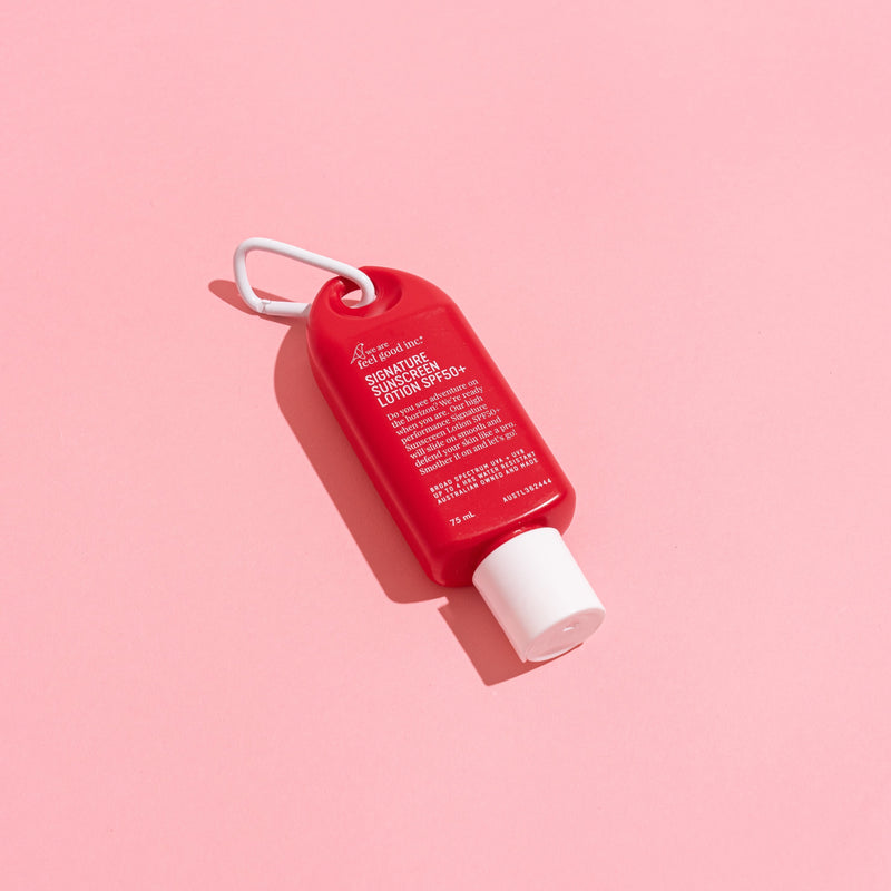 A small red hand sunscreen bottle with a white cap and a white loop keychain, photographed on a solid pink background.