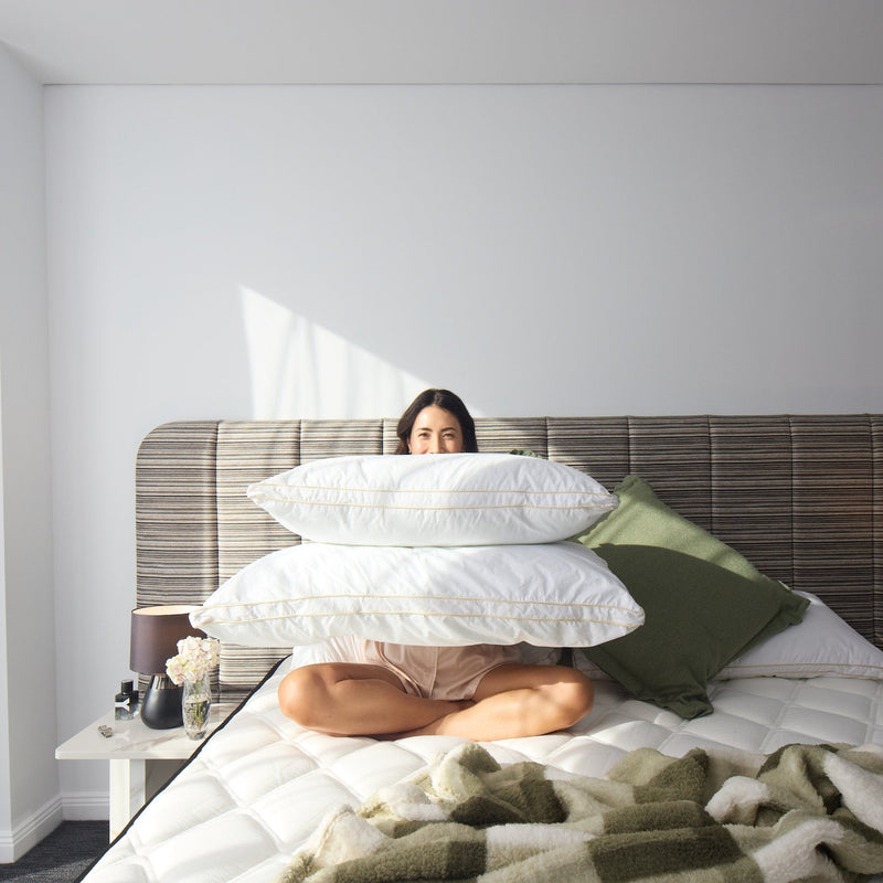 Woman sitting on a bed with a stack of pillows in a modern bedroom.