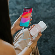 Person holding a smartphone and a portable power bank with a blurred background. Shop Meriton Suites SnapWirless